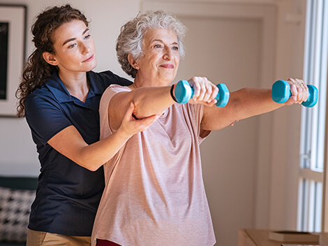 A therapist assisting an elderly patient with lifting small weights for shoulder and arm therapy.
