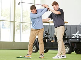 A guy works on  the form of his golf swing with the help of an instructor.