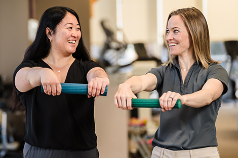 A patient and her physical therapist smile at each other while completing arm exercises.