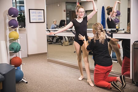 Therapist assisting dancer positioned in ballet pose