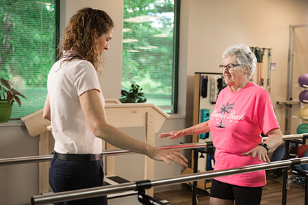 Therapist facing patient balancing between parallel bars