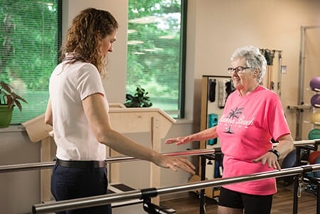 Therapist facing patient balancing between parallel bars