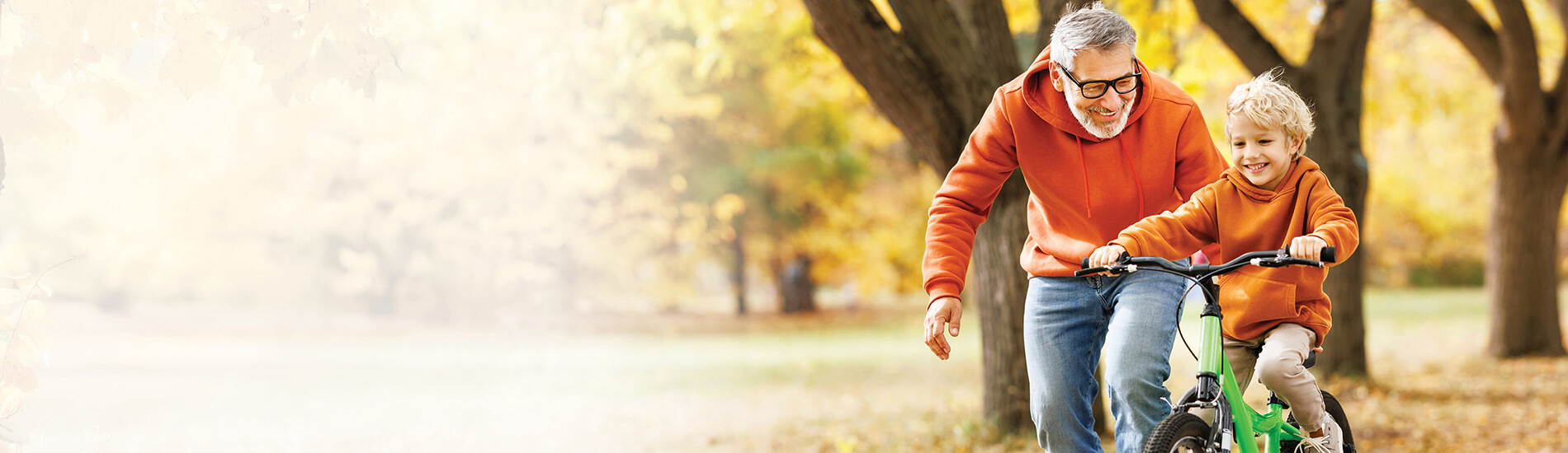 Man teaching his son to ride a bike, with yellow Autumn trees in the background.
