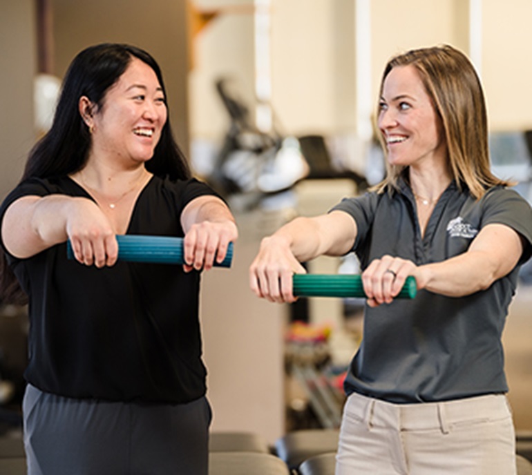 Female therapist working with a female patient on hand exercises inside of a physical therapy center.