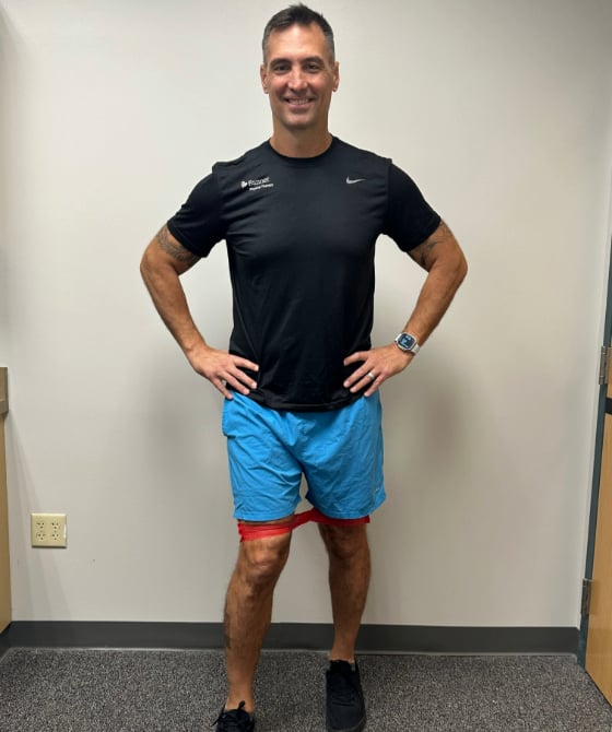 A male physical therapist with an exercise band around his quads with his right leg stretched out in front. . 