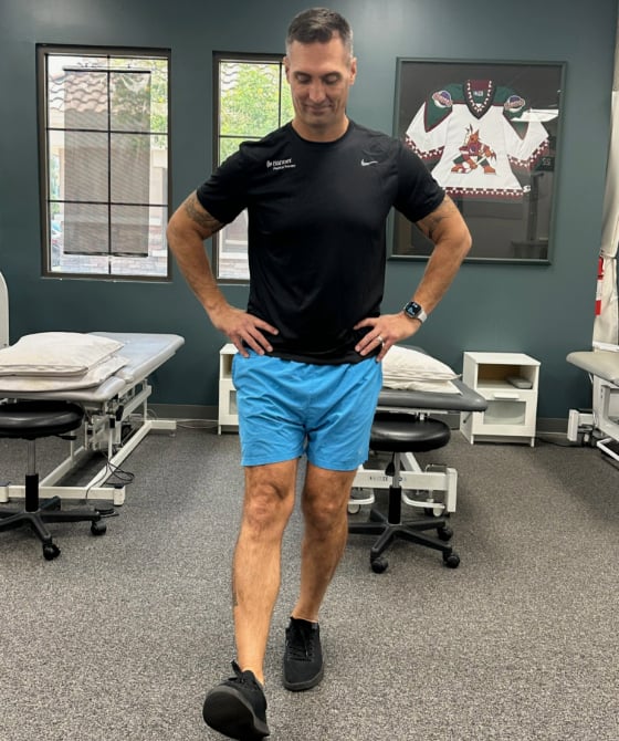 A male physical therapist with his right leg stretched forward in the air. 