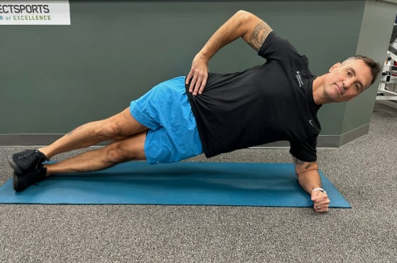 A male physical therapist on a yoga mat in a side plank position. 