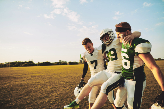 An injured football player getting carried off the field by his teammates. 