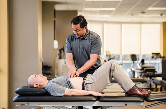 A patient is laying on his back on a table while a therapist is pressing on their torso