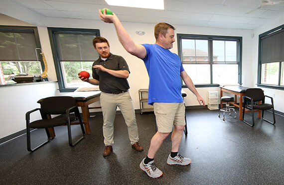 Physical therapist is helping an athlete practice proper throwing form inside