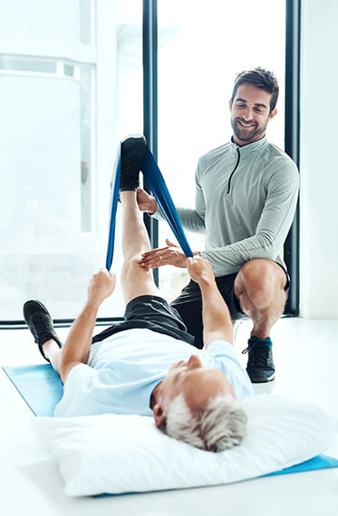 Alternate viewpoint of patient laying on floor to performing banded exercises for knee with help of therapist