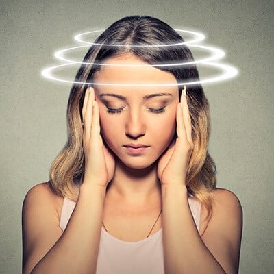 Young female, eyes closed, holding her hands at the temples with imaginary white rings circling her head.