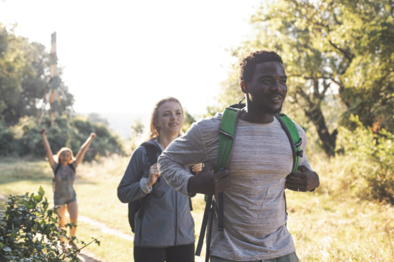 A group of adults hiking and smiling through the woods. 