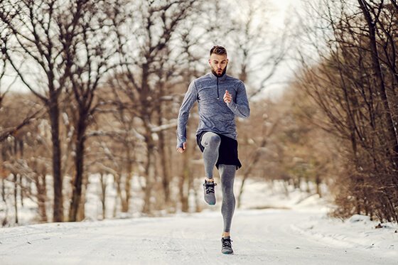 Young man stretching his legs outdoors in the snow.