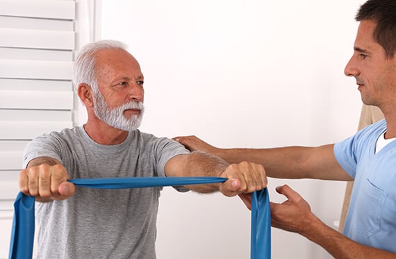 Patient using a band for upper body exercise with the help of a physical therapist