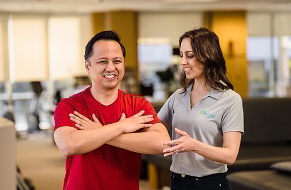 Patient is performing an exercise with arms in a crossed position. Therapist is beside him helping with posture.