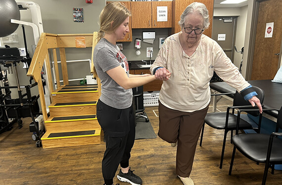 Karen balancing on one leg with the support of occupational therapist Olivia