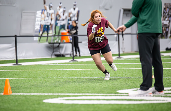 Athlete running across field while athletic trainer tracks the time