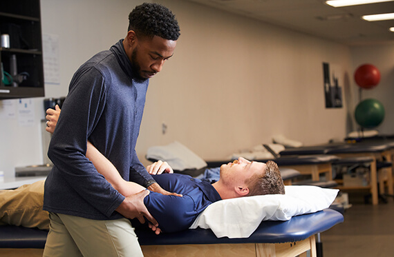 Patient is laying on exam table while physical therapist checks their shoulder