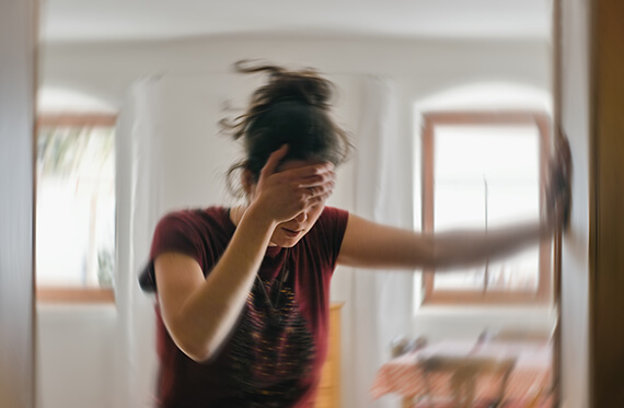 Blurred image of a dizzy women leaning against a wall and holding her head in one hand