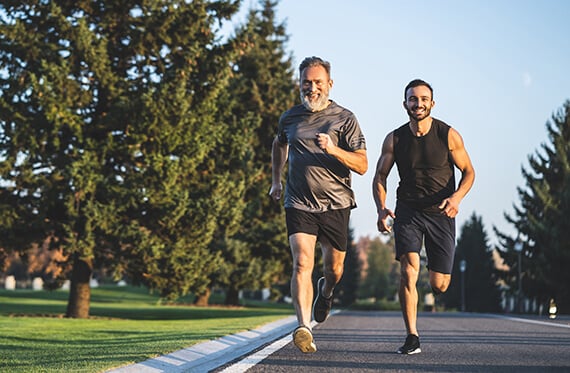 Two men running along a road outside in warm weather