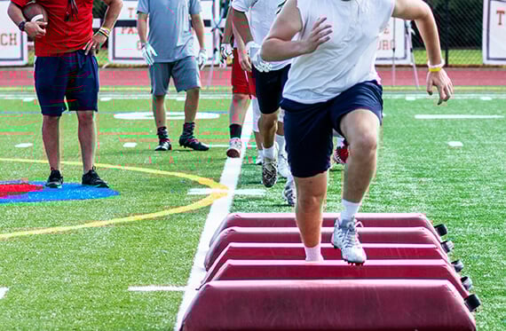 A group of men running footwork drills on a football field