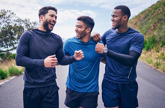 Three men outdoors in workout clothes fist bumping and smiling