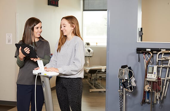 A therapist and patient are standing beside each other while the therapist shows the patient something on an ipad