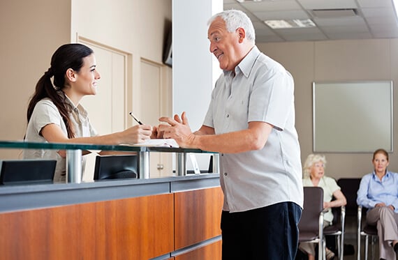 An man is standing at a receptionist desk while the receptionist is smiling at him