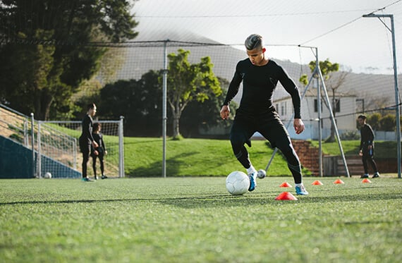Soccer player is completing a dribbling drill around cones on a soccer field