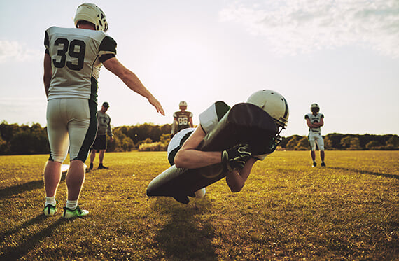 A group of football platers are standing around a player that is tackling a dummy