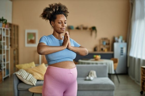 A pregnant Black woman doing breathing exercises in her living room. 