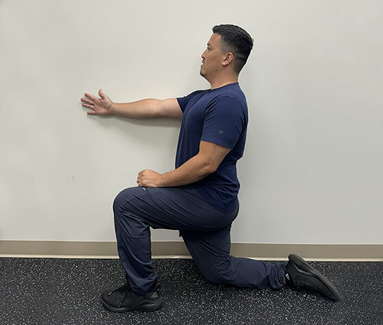 A male physical therapist in windmill position one, with his right arm flat against a wall. 