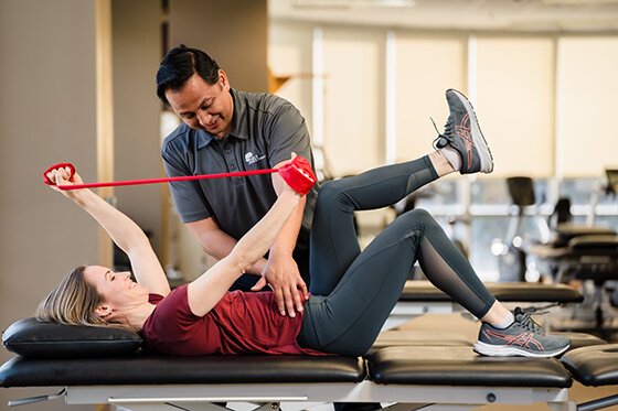 A therapist instructing a woman on how to exercise using a physical therapy resistance band.