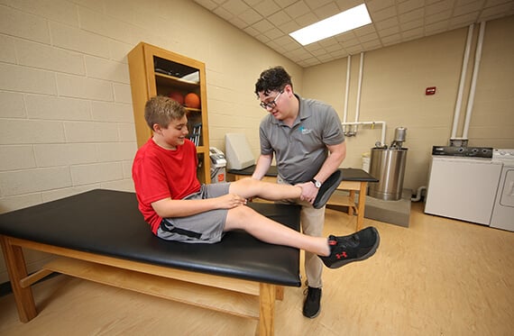 Athlete sitting on exam table while athletic trainer examines leg