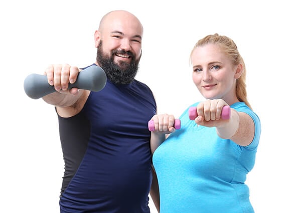 A man and women stand beside each other smiling and holding weights towards the camera